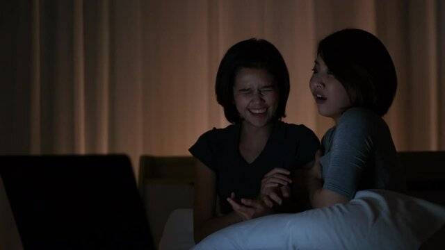 Two woman watch scary movie via laptop in bedroom and they action of frightening from some scene in the movie. Concept of entertainment with friend at home.