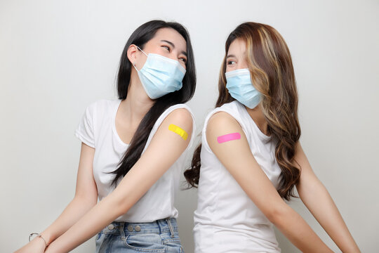 Smiling Of Asian Women Show Bandage On Arm. Happy Women Feel Good After Received Covid-19 Vaccine With Copy Space On White Background.