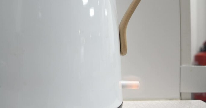 Shot of a hand clicking on a white kettle to boil, red light on the kettle switch.