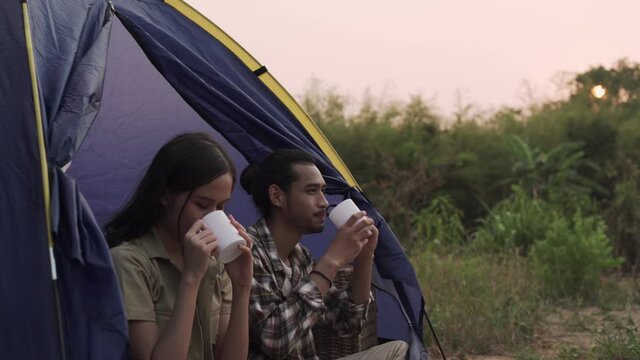 A couple is having an evening on vacation. Men and girlfriends are enjoying drink and nature while camping. Recreation and camping concept.
