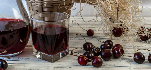 Cherry and cherry juice or wine on a wooden table, a decanter and a glass with juice, a basket with...