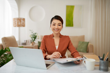 attractive young businesswoman using laptop and smiling at camera while working