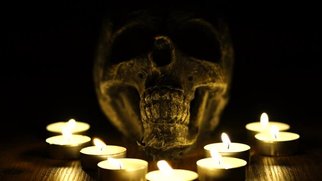 Creepy skull for halloween ceremony in the dark. A view of a skull for black ceremony ritual and lighting white candles that are symmetrical placed in the dark.