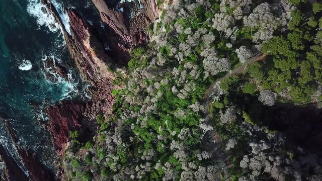 Aerial top down over a rugged cliff coastline slides to the right to reveal cliffs and rough oceans on the opposite side, in Eden Australia