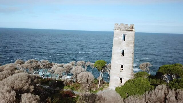 Aerial shot flying a 360 around an old stone whaling tower standing tall next to the ocean, at Eden Australia