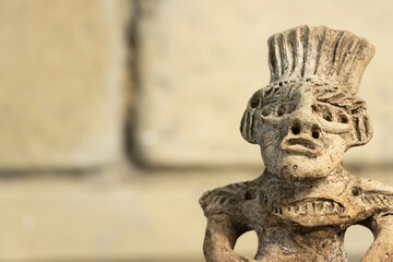 Statue of an Aztec warrior made of clay in front of an adobe background