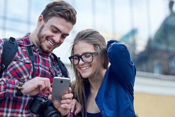 Fototapeta premium Happy couple with smart phone. Happy young loving couple standing outdoors together and looking at the mobile phone together