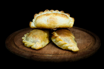 Baked empanadas, on a wooden plate, typical Argentine food. Black background