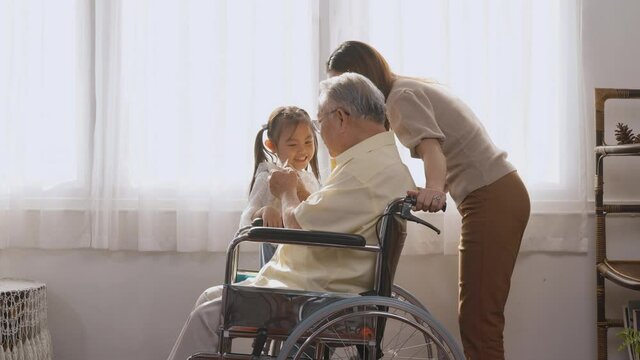 Asian happy disabled elderly in wheelchair with daughter and granddaughter smiling playing together in living room at home, family visit to support old senior man