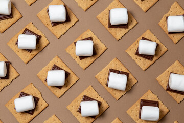 s'mores ingredients. graham cracker squares with chocolate, marshmallows on a brown background....