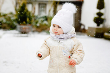 Happy little baby girl making first steps outdoors in winter through snow. Cute toddler learning walking. Child having fun on cold snowy day. Baby's first snow, activity. Winter walk outdoors