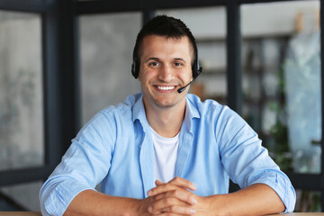 Portrait of a young smiling employee support services in the headset looking at the camera, online...