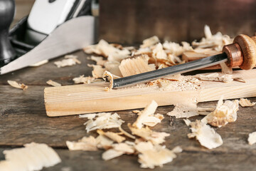 Carpenter's chisel, wooden plank and saw dust on wooden background, closeup