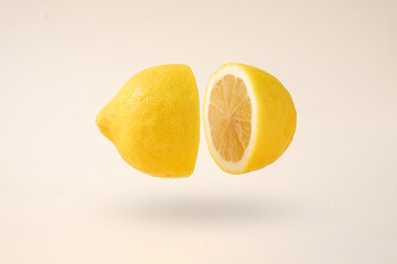 The idea of splitting into two and levitation. A cut lemon in levitation flies freely over a creamy background. Contemporary minimal concept.
