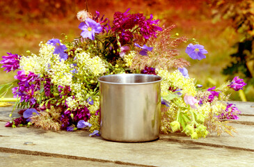 Metal mug stands on wooden table beside her lay a bouquet