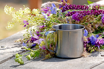 Cup of iron stands on a gray wooden table with flowers