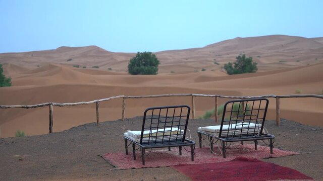 A man wears short and a rain jacket in the desert near unusable sunbed on a rainy day
