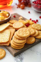 Board with tasty crackers with cheese and snacks on light background