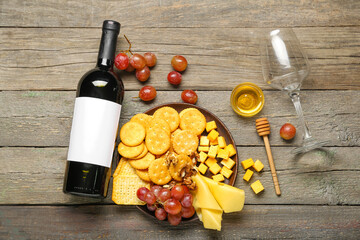 Plate with tasty crackers with cheese, snacks and wine on wooden background