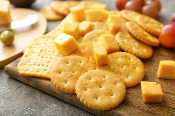 Board with tasty crackers with cheese on grey background