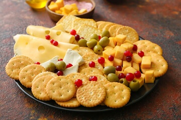 Plate with tasty crackers with cheese and snacks on grunge background
