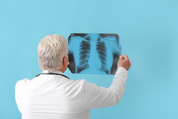 Senior doctor with x-ray image of lungs on color background