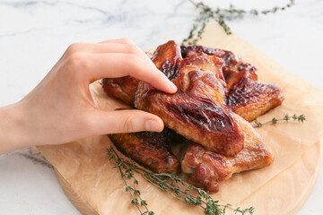 Woman eating roasted chicken wings on light background