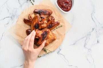 Woman eating roasted chicken wings on light background