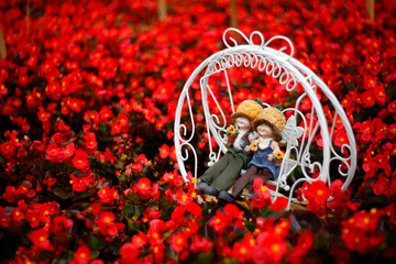 A pair of little lovers, sitting on a white rocking chair in a garden full of red flowers