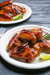 Plates with roasted chicken wings on dark wooden background