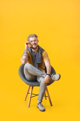 Fototapeta premium Handsome young man sitting in armchair on color background