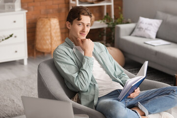 Young man reading book while sitting in armchair at home