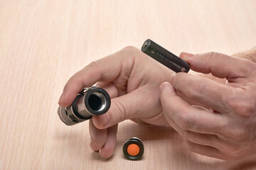 Hands hold a small black flashlight and replace the battery in it
