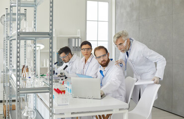 Obraz premium Senior male supervisor and young scientist assistant group discussing experiment test result looking at laptop screen. Researchers team developing new drugs working at pharmacy laboratory