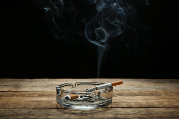 Ash tray with cigarettes on table against dark background