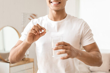 African-American teenage boy taking fish oil pill at home