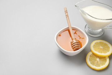 Bowl with sweet honey, lemon slices and jug of milk on grey background