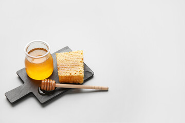 Glass jar with sweet honey, comb and dipper on board against grey background