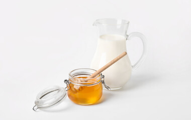 Glass jar with sweet honey jug of milk on white background