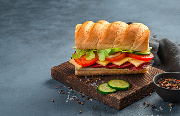 Sandwich with sausage, tomato, cheese and cucumber on a dark blue background.