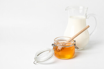 Glass jar with sweet honey jug of milk on white background