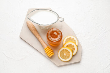Fototapeta na wymiar Glass jar with sweet honey, dipper, lemon slices and jug of milk on white background