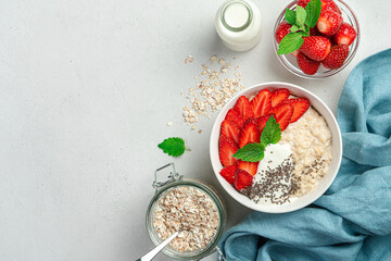 Oatmeal porridge with strawberries and chia seeds and ingredients on a gray background with space to copy.