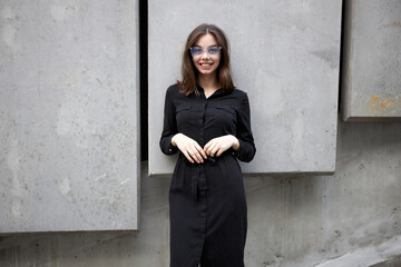 Fashion portrait of a sexy brunette woman with a make up wearing black clothes. She is wearing black modern dress, white sneakers and glasses