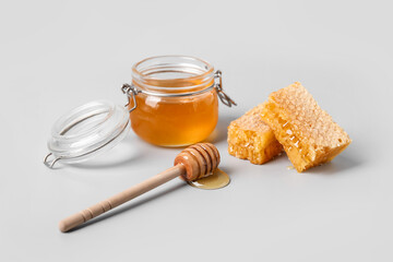 Glass jar with sweet honey, dipper and combs on grey background
