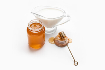 Glass jar with sweet honey, dipper and jug of milk on white background