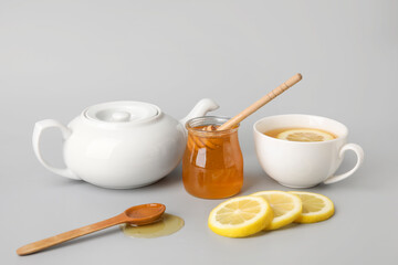 Glass jar with sweet honey, cup of tea and lemon slices on grey background