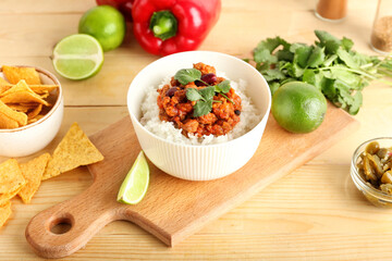 Bowl with tasty chili con carne, rice, lime and nachos on wooden background
