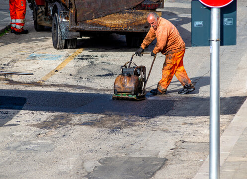 worker leveling fresh asphalt during asphalt pavement repair or construction works