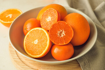 Plate with healthy oranges and tangerines on light background